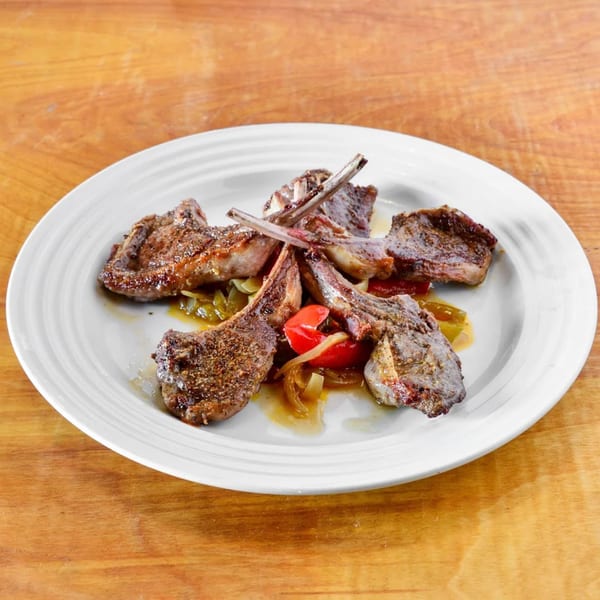 Grilled lamb chops with sautéed onions and red peppers on a white plate.
