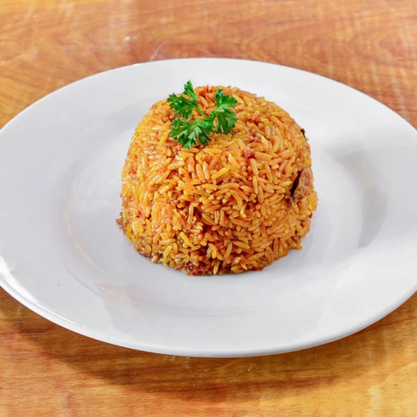 A mound of orange African Jollof rice, garnished with fresh parsley, on a white plate.
