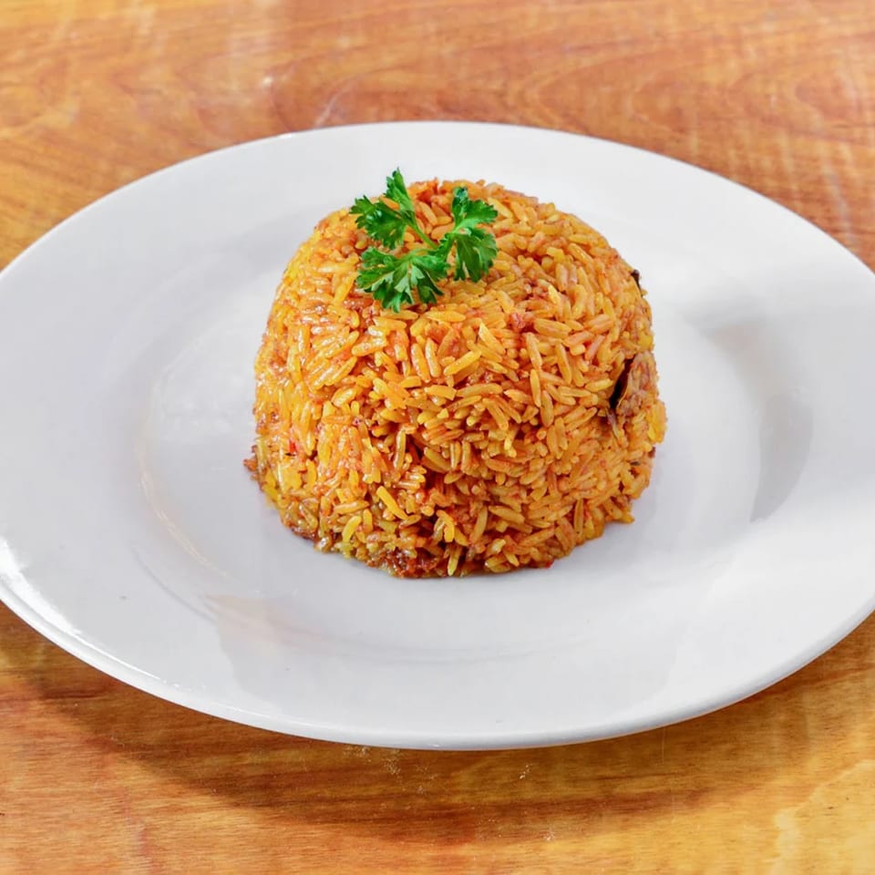 A mound of orange African Jollof rice, garnished with fresh parsley, on a white plate.