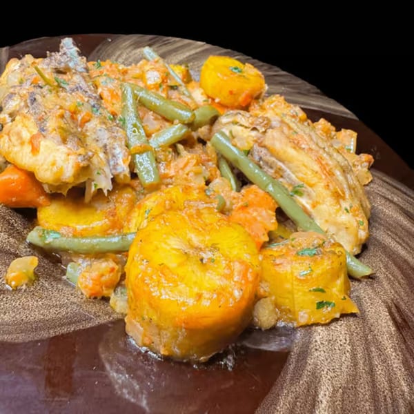 African dish with fish, plantains, green beans, and carrots in a creamy sauce on a brown plate.