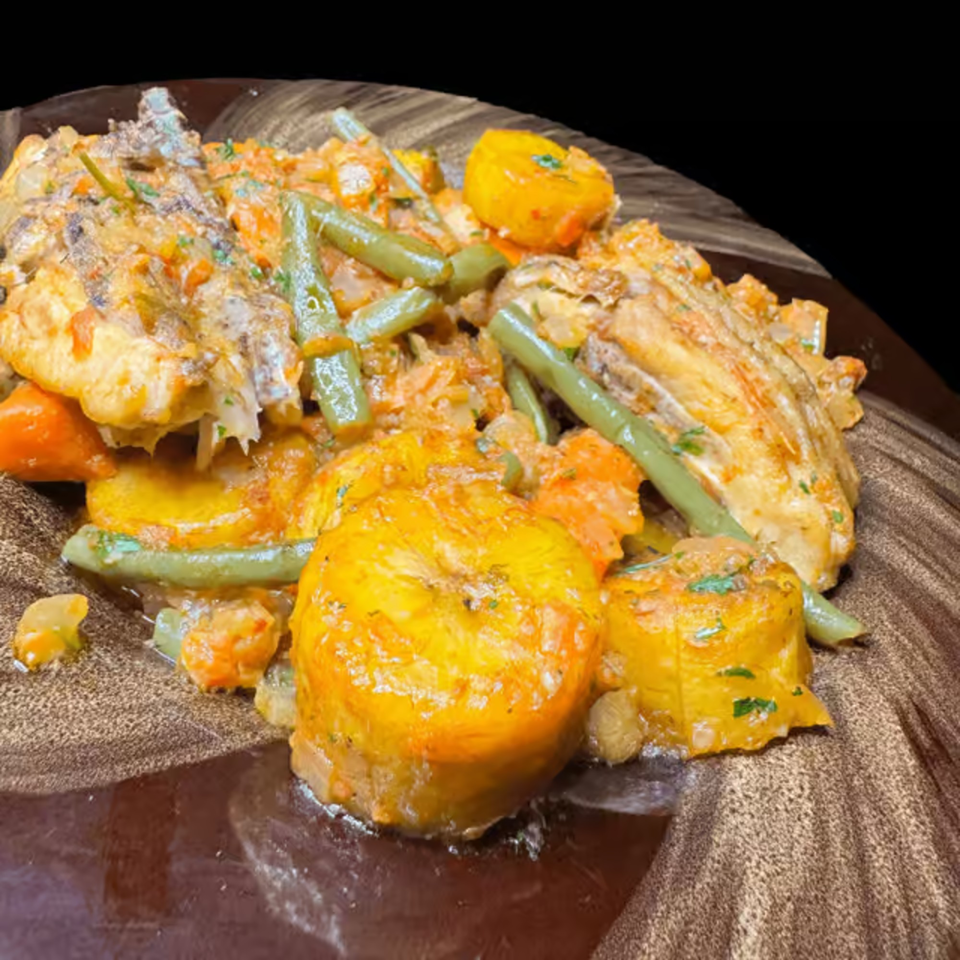 African dish with fish, plantains, green beans, and carrots in a creamy sauce on a brown plate.