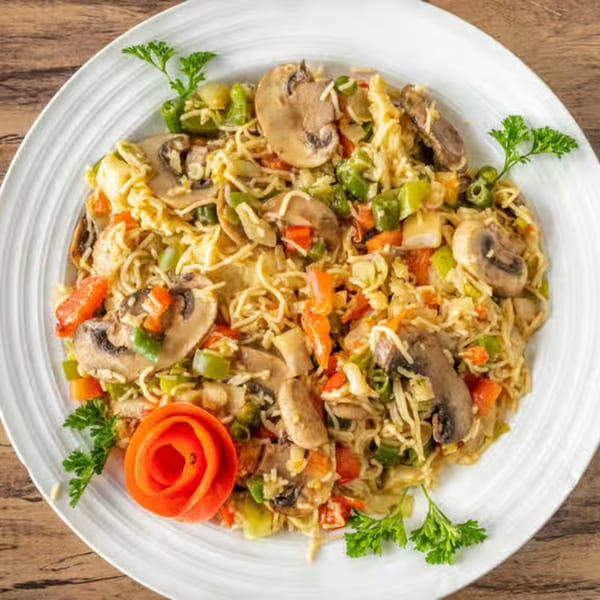 African noodles with mushrooms, bell peppers, and carrots, garnished with parsley and a tomato rose.