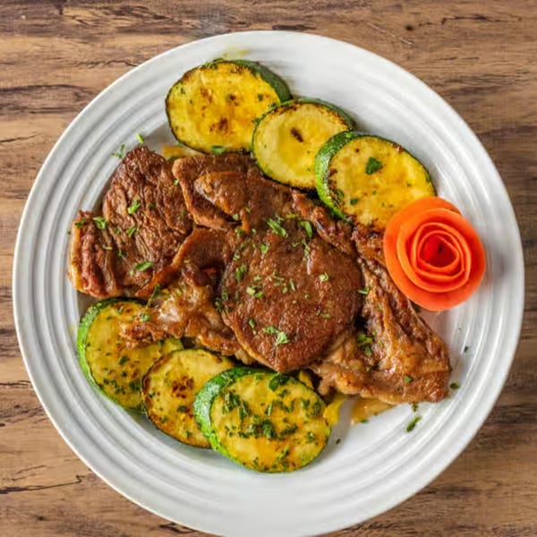 Grilled meat with zucchini slices and a carrot garnish on a white plate, from Choukouya Resto-Bar.