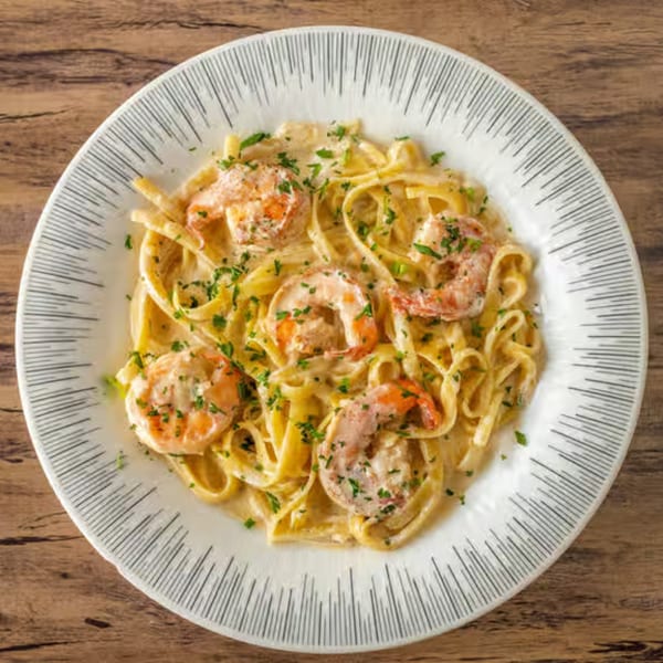 Creamy pasta with shrimp and parsley on a white plate with black stripes, on a wooden table.